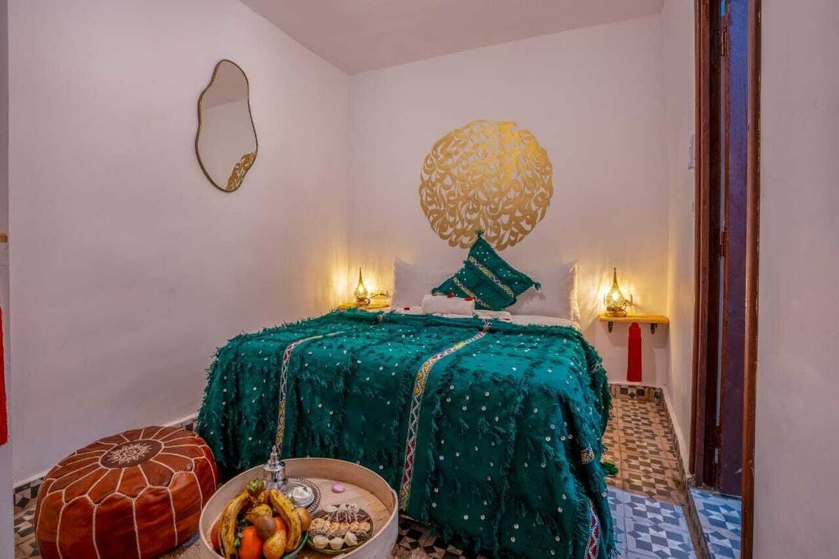 Una habitación acogedora con una cama, un adorno en la pared y una mesita con frutas y frutos secos.