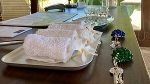 Un escritorio de madera con una computadora portátil, una lámpara, una bandeja con toallas, un vaso de agua y una pequeña planta.