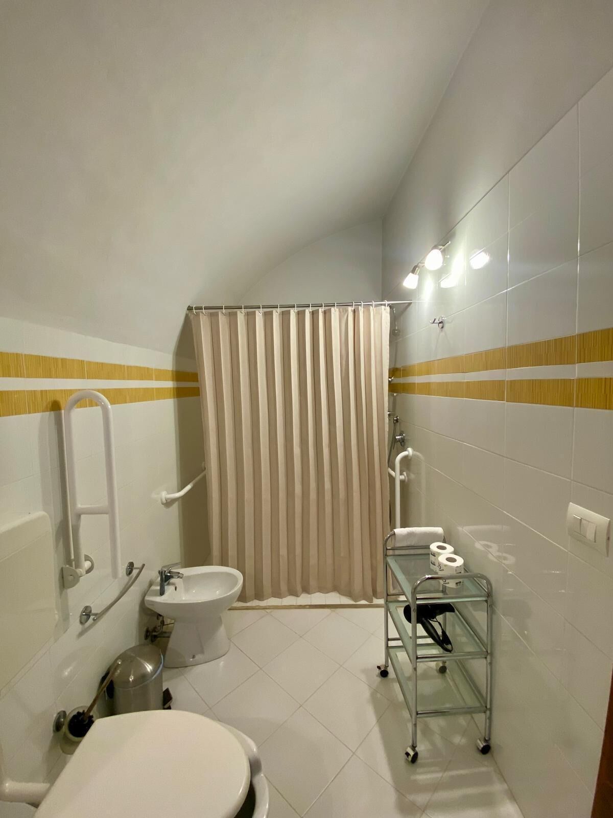 A small bathroom with a toilet, bidet, and a glass shelf with toiletries.