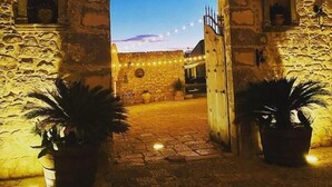 Una entrada de piedra arqueada con macetas a cada lado, que conduce a un patio con luces colgantes.