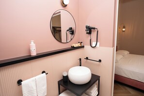 Ein Badezimmer mit rundem Spiegel, Waschbecken, Handtuchhalter und einem Föhn an der Wand.