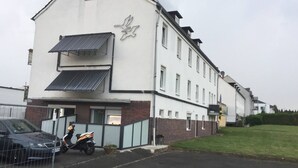 Un edificio de dos pisos con fachada blanca y un logotipo en el lateral. Hay una scooter estacionada y un automóvil frente al edificio.