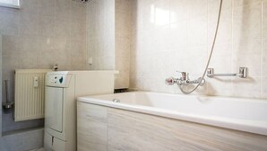 Un baño con una bañera blanca, inodoro empotrado y radiador fijado a la pared.
