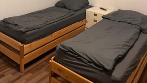 Una habitación pequeña con dos camas de madera, una mesita de noche blanca y un equipo de aire acondicionado instalado en la pared.