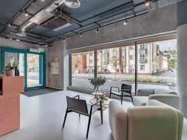 A modern lobby with a reception desk, seating area, and large windows offering a view of the street and buildings.