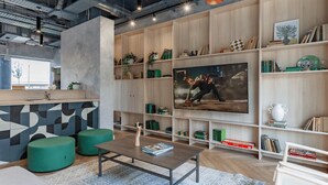Een moderne woonkamer met een grote flatscreen televisie, houten boekenkasten en groene poefs.