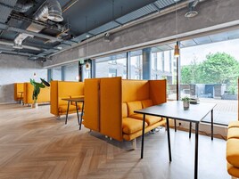 A modern office space with orange seating, large windows, and a herringbone wood floor.
