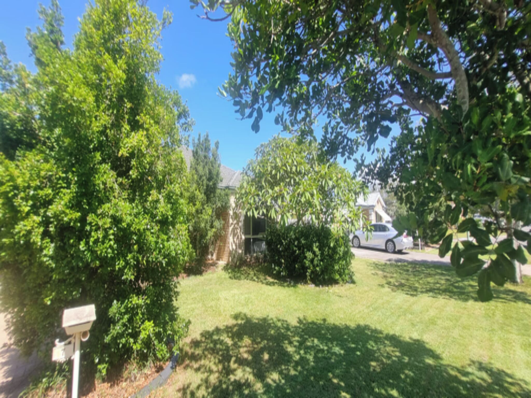 A residential area with a white car parked on the street, surrounded by lush green trees and a well-maintained lawn.