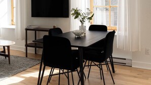 A dining area with a wooden table, black chairs, a flat-screen TV, and a window with curtains. - Maison Rasco • One-Bedroom Apartment • Old Montreal • Central • Self Check-In Access • Full Kitchen • Pet Friendly • Wi-Fi • AC (Montreal)