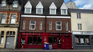 Un edificio de ladrillo de dos pisos con fachada roja que dice 'TICK TOCK CAFE' y un letrero para 'MIRACLE SKINCARE CENTRE' a la derecha.