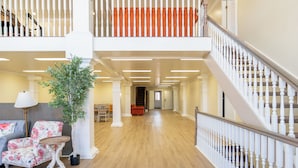 Un intérieur spacieux doté d’un plancher en bois, d’un escalier avec des balustrades blanches et d’un coin salon avec des fauteuils à motifs floraux.