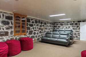 Una habitación con pared de piedra, sofá de cuero gris, pufs rojos y un armario de madera.