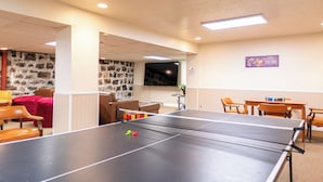 Une table de ping-pong dans une pièce avec un mur en pierre, un téléviseur et un panneau indiquant « Moment en famille ».