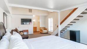 Une chambre à coucher avec un grand lit, une chaise, une petite table et un téléviseur fixé au mur.
