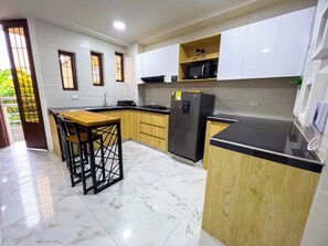 A kitchen with wooden cabinets, a marble floor, a refrigerator, and a bar stool. - AMGES (Tumaco)