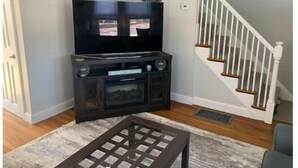 Una sala de estar con televisor, centro de entretenimiento y una escalera.