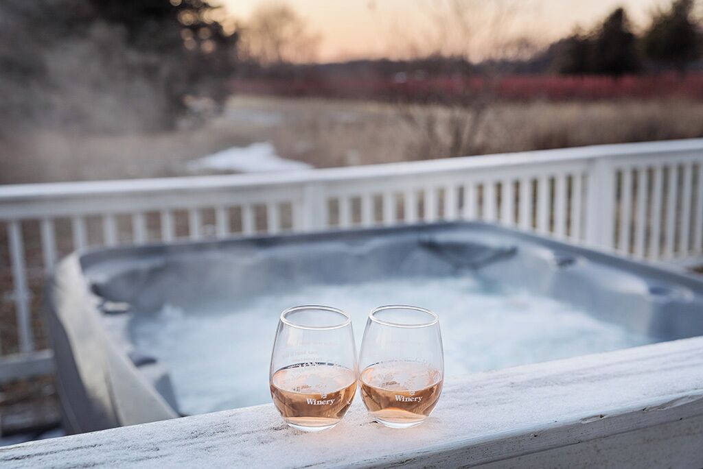 Dos copas de vino sobre una barandilla blanca, con un jacuzzi al fondo.