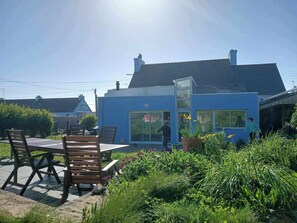 Una moderna casa blu con un'ampia porta in vetro, un patio con mobili in legno e un giardino con diverse piante.