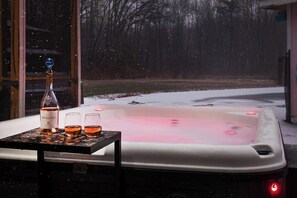 A hot tub with a bottle and glasses on a table, a window, and a snowy outdoor scene. - Pool & Pond | Hot Tub | 2 Acres | Pond | Ping Pong (Bridgman)