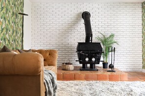 A living room with a brick fireplace, a brown sofa, a white rug, and a potted plant.
