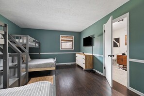 A room with bunk beds, a desk, a TV, and a door leading to another room.