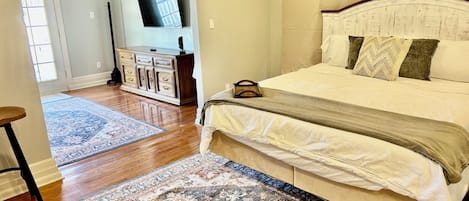Une chambre avec un grand lit, une commode, un téléviseur fixé au mur et un tapis à motifs sur le sol.