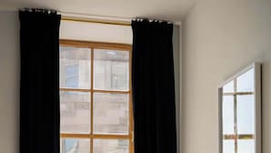 Una habitación con una cama, cortinas negras, un ventanal y un cuadro en la pared.