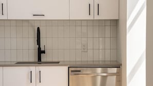 Una cocina con alacenas blancas, un lavavajillas de acero inoxidable y un salpicadero de azulejos.