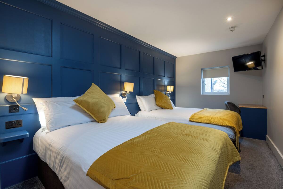 Een hotelkamer met twee bedden, een aan de muur bevestigde televisie en een bureau met stoel.