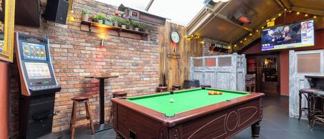 A billiards table in a room with brick walls, a digital jukebox, and a television screen displaying a boxing match.