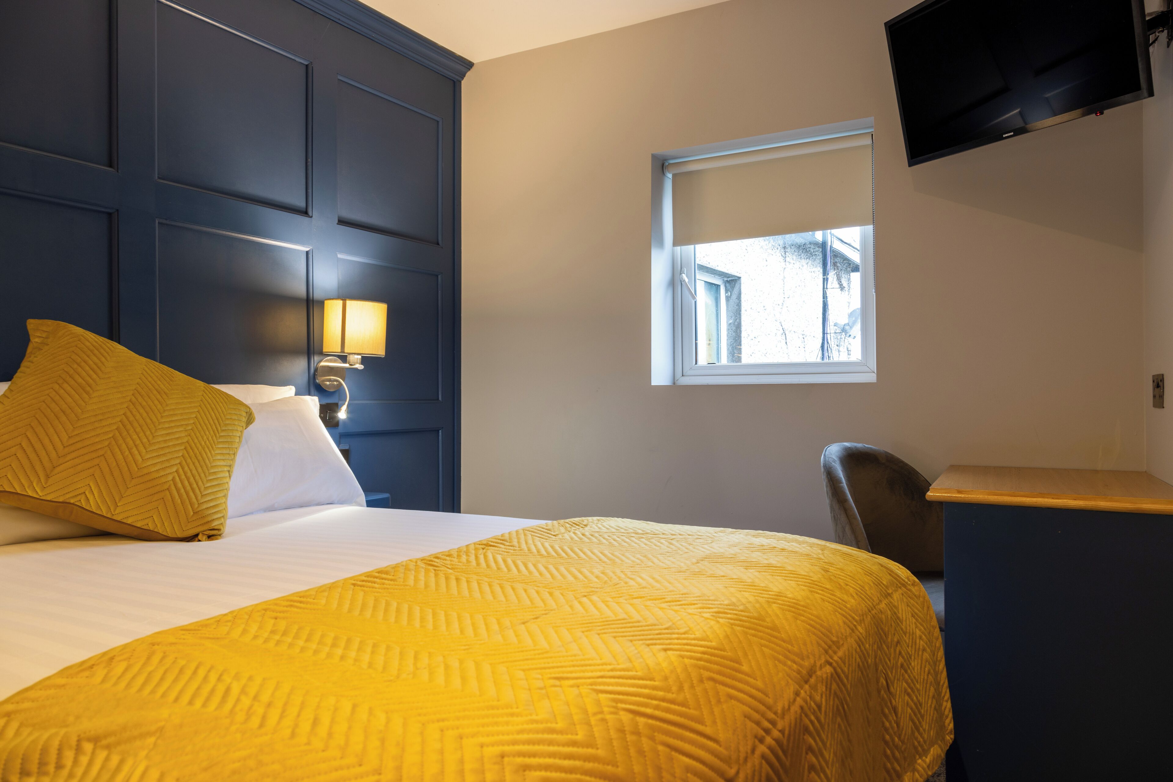 Habitación de hotel con cama, escritorio, silla, televisor y ventana.