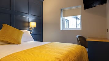 Habitación de hotel con cama, escritorio, silla, televisor y ventana.