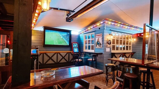 A cozy bar with wooden furniture, a large TV screen, and Guinness branding. - Ewings Bar & Self-Catering Accommodation (Carlow)