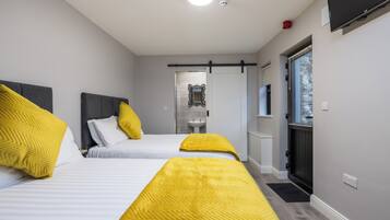 A hotel room with two beds, a television, a sink, and a window with blinds.