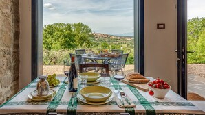 A dining table set with plates, glasses, and a bottle, overlooking a scenic landscape.