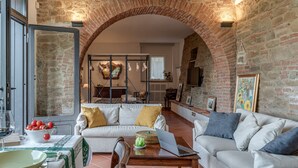 A cozy living room with a fireplace, two sofas, a dining table with a bowl of fruit, and a laptop.