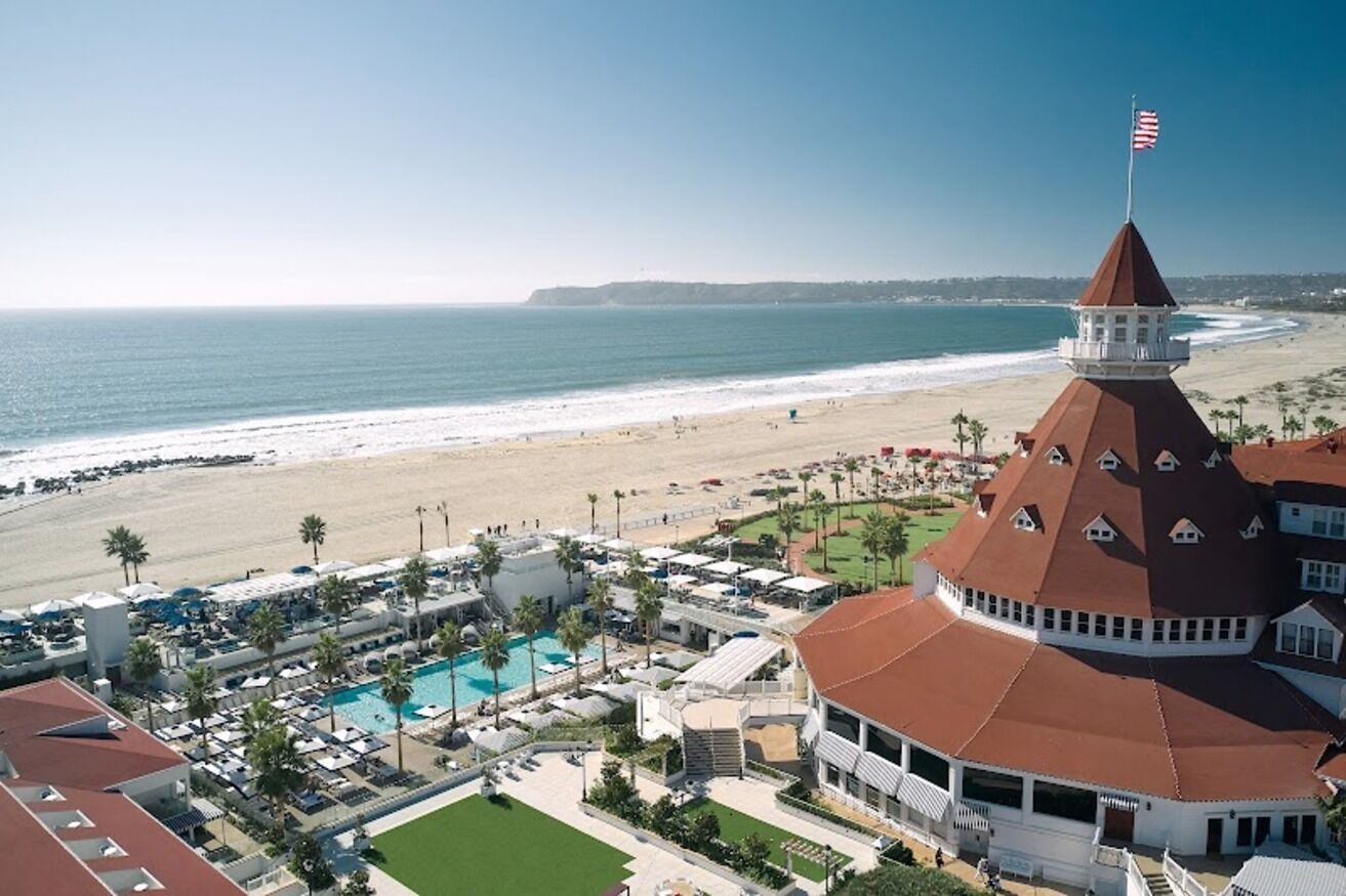 A coastal hotel with a swimming pool, beach view, and a distinctive tower with an American flag.