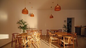 Un comedor amplio con varias mesas y sillas de madera, lámparas colgantes y una planta en maceta.