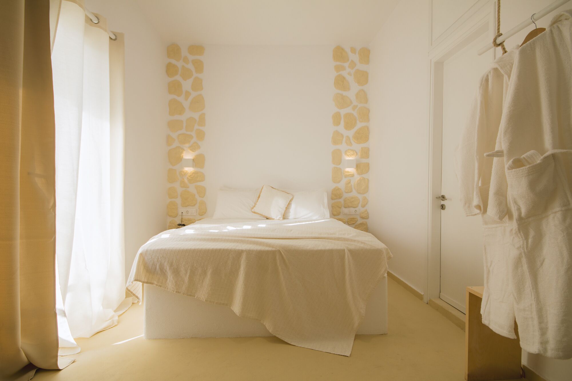 Een slaapkamer met een bed, een stenen muur, een deur en een handdoekrek.