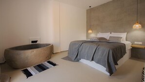 Un dormitorio moderno con una bañera grande, una cama con colcha gris y dos lámparas colgantes.