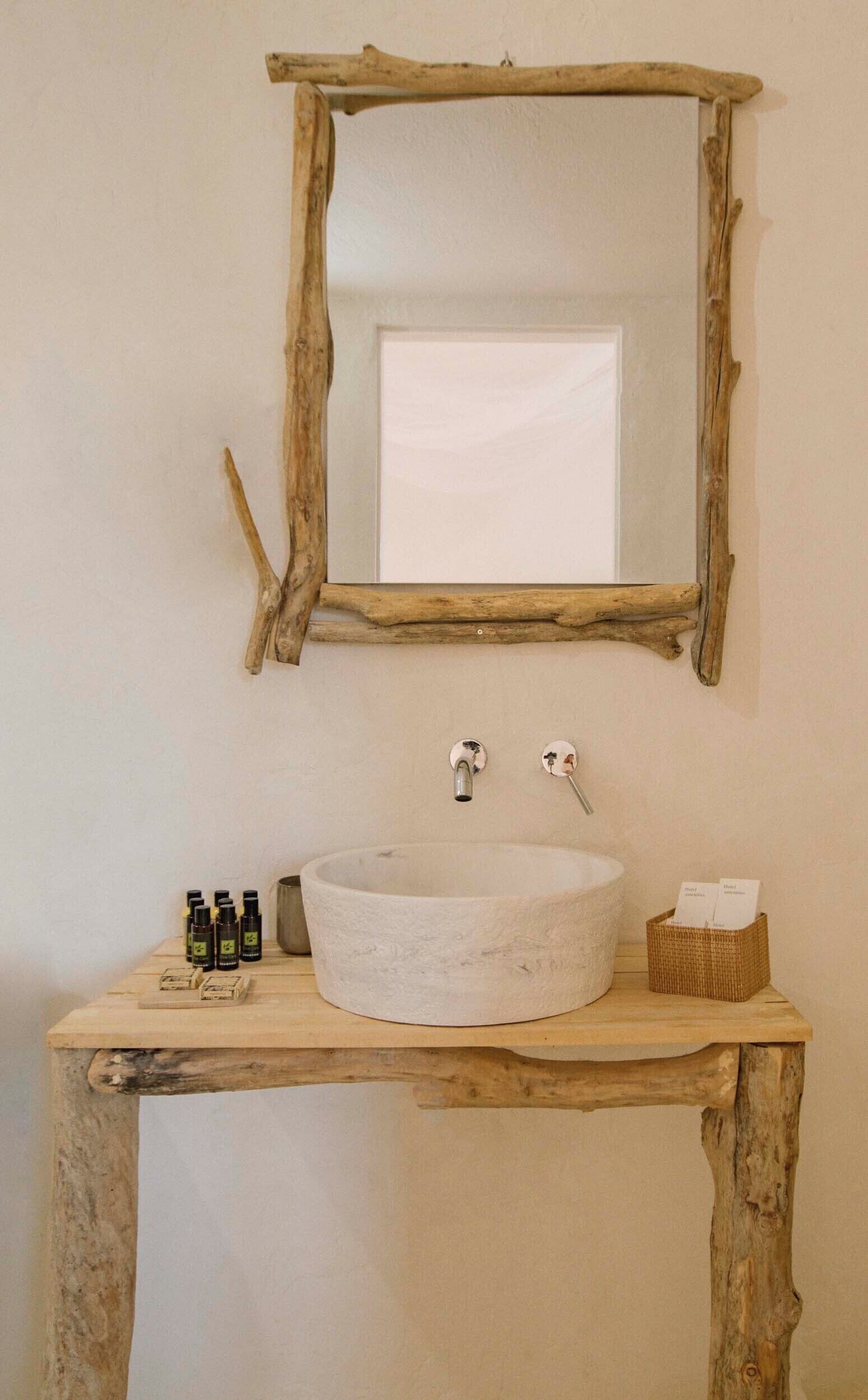 Une salle de bain rustique avec un grand lavabo rond et blanc, un miroir encadré en bois et une petite étagère en bois où sont posés les articles de toilette.