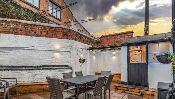A patio area with a brick wall, a table with chairs, and a small laundry room with a washing machine. - Spacious home, sleeps 9 - walker & cyclist retreat -Pass the Keys (Shropshire)