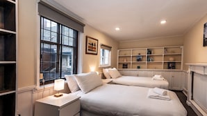 A bedroom with two beds, a bedside table with a lamp, a bookshelf, and a window with blinds. - Spacious home, sleeps 9 - walker & cyclist retreat -Pass the Keys (Shropshire)