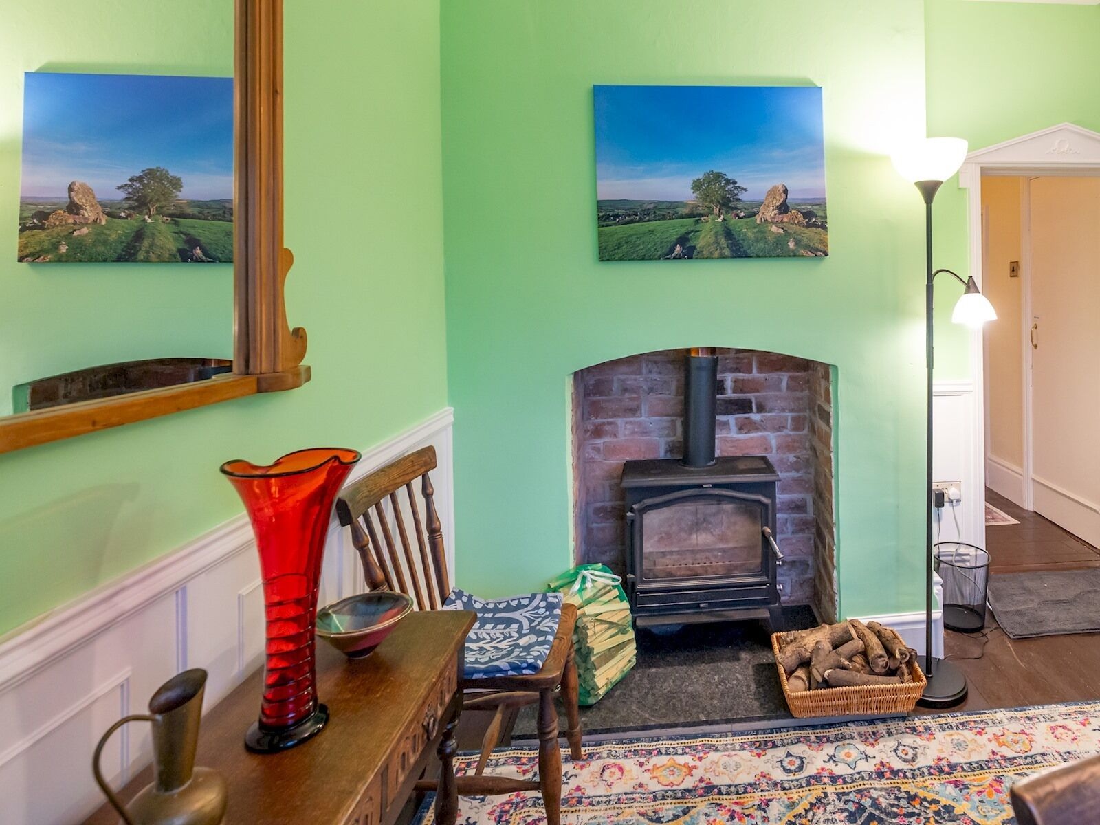 A living room with a fireplace, a wooden chair, a red vase, and a rug.