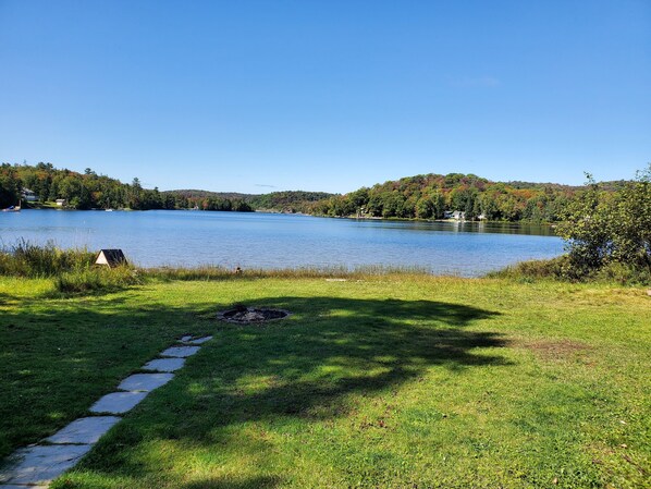 A lakeside property with a stone pathway leading to a grassy area, surrounded by trees and hills.