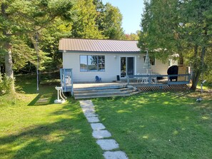 A small cabin with a porch, a basketball hoop, and a swing set.