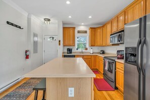A modern kitchen with wooden cabinets, stainless steel appliances, and a central island. - Mountain Views + Walk to Overlook Barn, Slopes, Fred's & White Wolf! (Banner Elk)