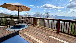 Une terrasse en bois avec une table et des chaises, un parasol et une vue sur les montagnes.