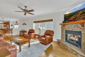 A spacious living room with leather armchairs, a coffee table, a fireplace, and a large window with a view of a mountainous landscape. - Mountain Views + Walk to Slopes, Overlook Barn, Fred's & White Wolf! (Banner Elk)