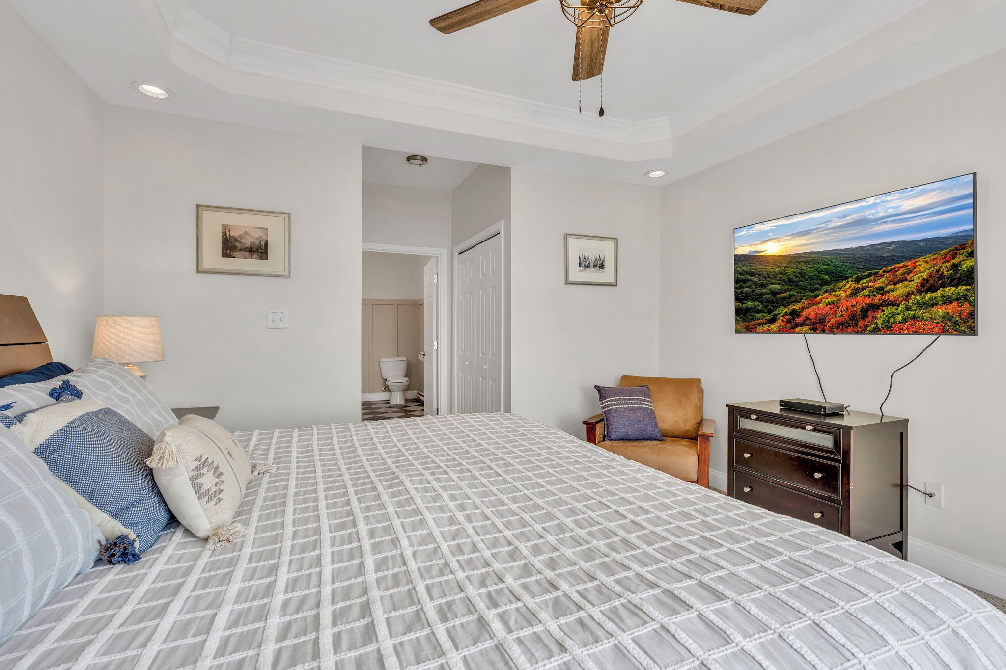 A bedroom with a bed, a television, a ceiling fan, and a door leading to a bathroom.